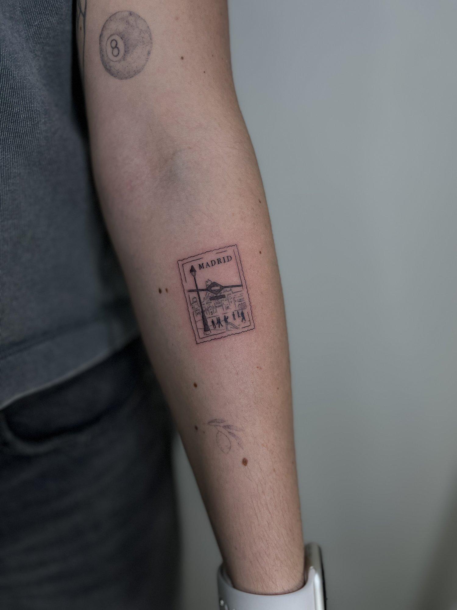 Tatuaje de sello postal madrid y bola och en antebrazo, línea fina