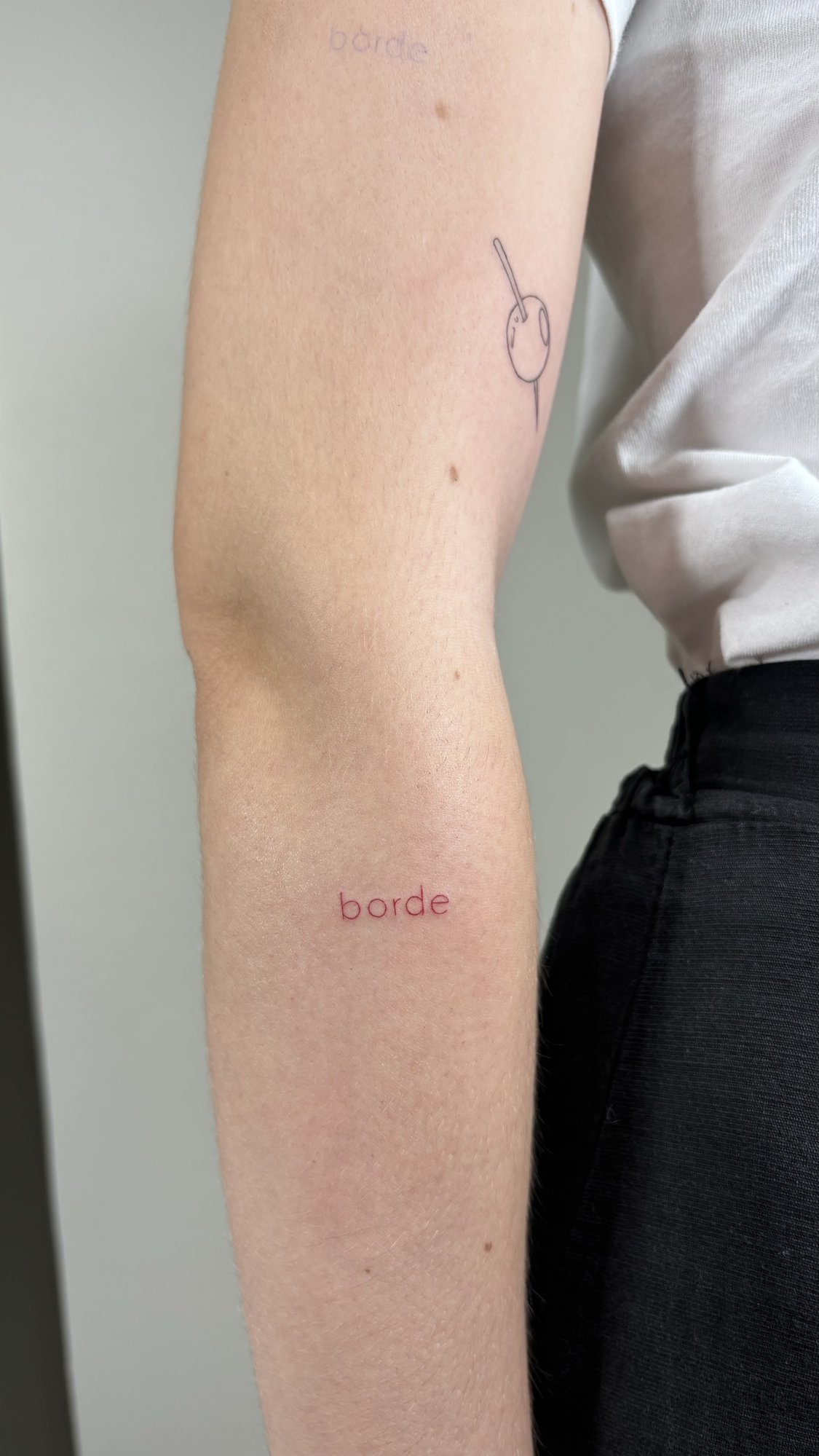 Tatuaje de texto borde y oliva aguja en brazo, línea fina